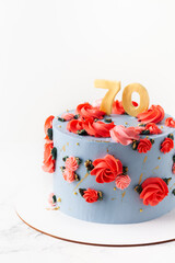 Birthday cake with blue cream cheese frosting decorated with red flowers on the white background