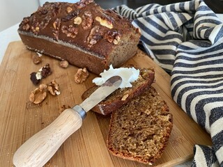 Homemade banana bread. Slice cut from a loaf on a cutting board and spread with curd cheese using a small serving knife with a wooden handle