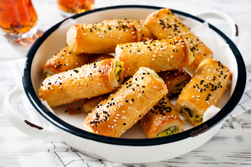 Turkish borek rolls with spinach and cheese. A traditional Turkish pastry rulo borek with black and white sesame seeds. White  wooden background.