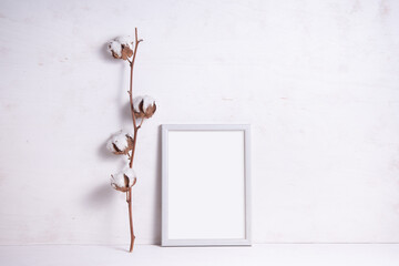 Photo frame decorated with cotton flower branch on white wooden background