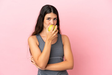 Young caucasian woman isolated on pink background eating an apple