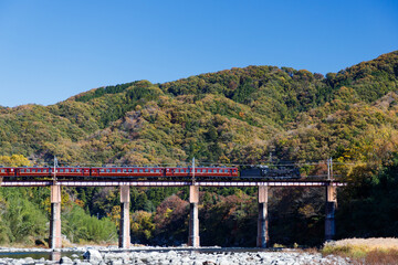 Fototapeta na wymiar 長瀞秩父鉄道、青空と山を背景に荒川橋梁を渡る蒸気機関車と客車
