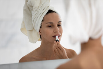 Head shot mirror reflection close up view attractive young hispanic mixed race woman applying favorite lipstick, doing makeup, getting ready, enjoying morning beauty routine after showering at home.