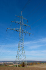 Stromversorgung: Strommast zwischen landwirtschaftlichen Feldern / Hochspannungsleitung / Hochspannungsmast (&Uuml;berlandleitung) vor einem blauen Himmel - Elektrizit&auml;t
