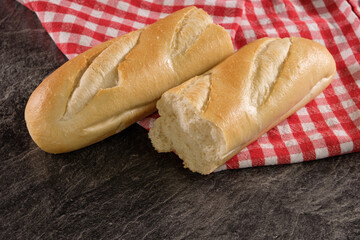 Französisches Baguette, aufgebrochen auf einem rot kariereten Tuch auf einer dunklen Küchenplatte 