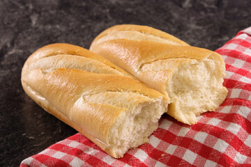 Französisches Baguette auf einem rot kariereten Tuch auf einer dunklen Küchenplatte 