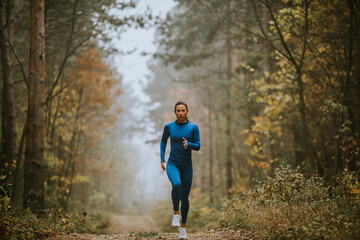 Fototapeta na wymiar Young woman running toward camera on the forest trail at autumn