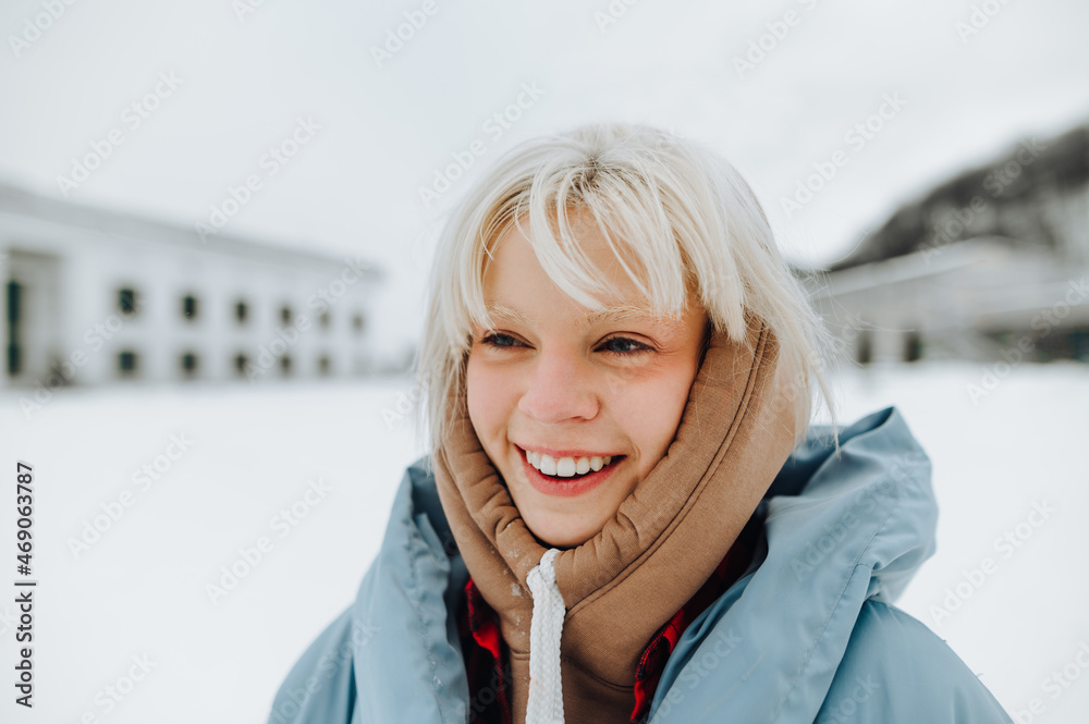 Wall mural portrait of a positive blonde girl with white eyebrows in warm clothes on a winter street, looking a