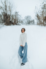 Fashionable winter photo of a stylish woman on a snowy street posing for the camera with a serious face. Vertical.