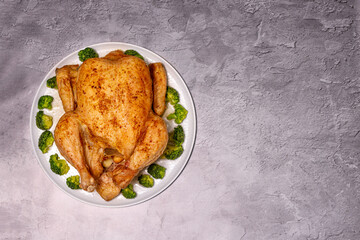 baked whole chicken with broccoli on a round dish on a gray background, copy space, top view