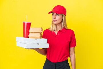 Delivery Uruguayan woman holding fast food isolated on yellow background looking to the side