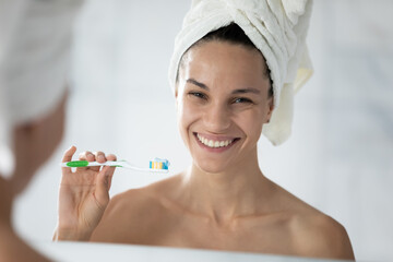Smiling attractive mixed race hispanic woman with towel on head looking at camera, holding toothbrush with whitening paste in hand, daily dental oral care domestic procedure, healthy teeth product ad.