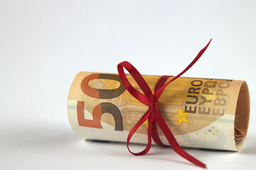red bow on a roll of 50 euro banknote on white background, cash gift concept