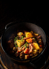 Goulash. Vegetable rague with meat, eggplant, pepper, potato and carrot in black bowl on dark wooden background