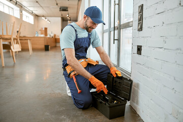 Male electrician using tool box to repair electrical socket - obrazy, fototapety, plakaty
