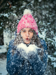 Cheerful girl in warm clothes plays with snow outdoors in the winter forest. Winter Holidays Concept