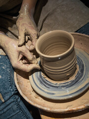 The female hands of a potter make a ceramic mug, made on a potter's wheel, working with soft and wet clay.