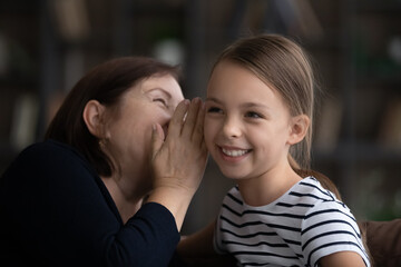Close up happy mature grandmother with little granddaughter gossiping, sharing secrets, senior...