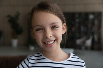 Head shot portrait of smiling 8s Caucasian girl child looking at camera, adorable happy kid having fun with webcam, making video call online, engaged in conference, blogger shooting recording