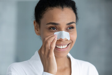 Head shot smiling attractive young african american biracial woman in bathrobe using nose cleansing...