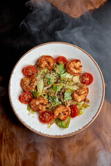 Salad on a plate with avocado and shrimp in smoke