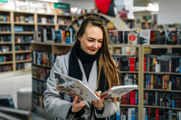 A beautiful young woman chooses a comic book for a gift in a bookstore to buy it. Stands in front...