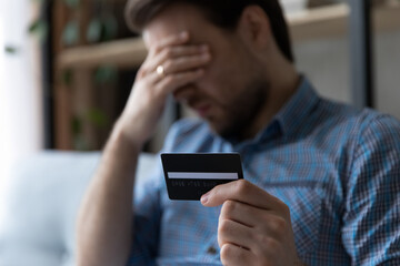 Depressed unhappy young man holding credit card in hands, feeling stressed having financial...