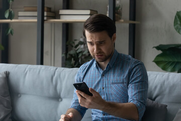 Stressed millennial generation man looking at cellphone screen, feeling anxious getting spam scam...