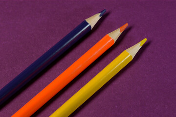 a simple image. three simple colored pencils on a purple background
