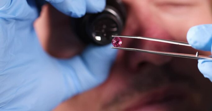 Jeweler holding pink diamond in hands and looking at it with magnifying glass closeup 4k movie slow motion