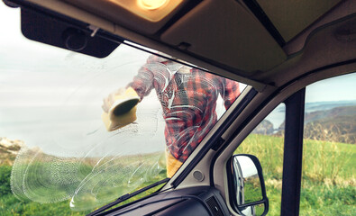 Unrecognizable man cleaning camper van windshield with sponge outdoor