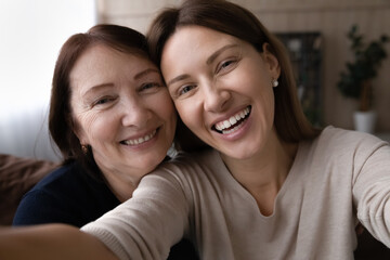 Head shot portrait happy woman with mature mother taking selfie on smartphone together, looking at...