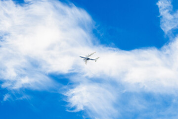 White plane in the blue sky. Clouds stretched by the wind.