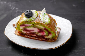 Pistachio roll decorated with blueberries lies on a saucer.