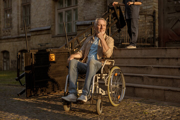 Obraz na płótnie Canvas Full length shot of cheerful mature disabled man in wheelchair smiling away while spending time alone outdoors at sunset