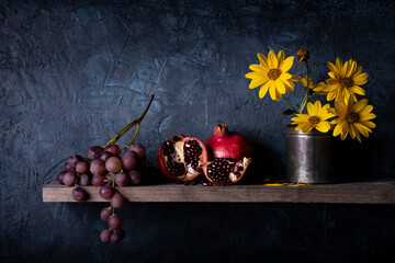 on the rustic wooden shelf, a bunch of grapes, pomegranates and yellow Jerusalem artichoke flowers. Still life © luigi giordano