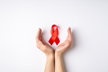 First person top view photo of cupped female hands and red ribbon symbol of aids awareness on...
