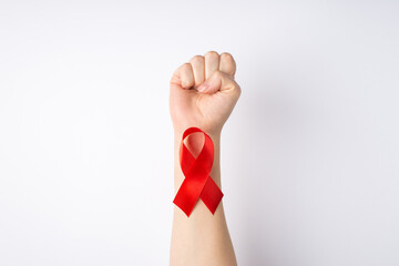 First person top view photo of raised female hand with clenched fist and red ribbon on wrist symbol of aids awareness on isolated white background