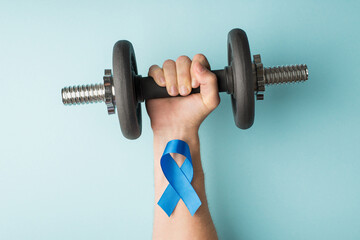 First person top view photo of raised man's hand holding dumbbell and blue ribbon on wrist symbol...