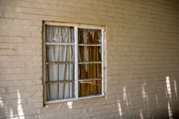 Window in a painted brick wall, the curtains in the window is busy disintegrating due to old age 