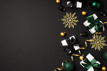 Top view photo of christmas decorations gold and black balls snowflakes small white gift boxes with green and black ribbon bows serpentine sequins on isolated black background with empty space