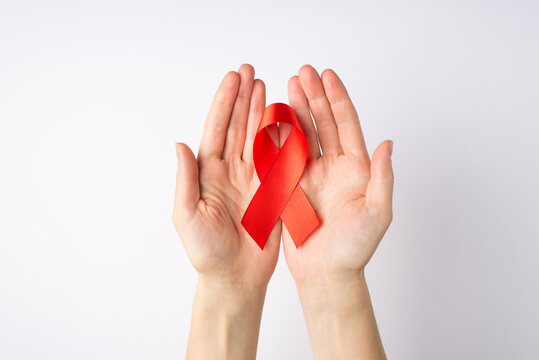 First person top view photo of young girl's hands holding red silk ribbon in palms symbol of aids awareness on isolated white background