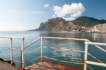 Koktebel resort village with Kara-Dag nature reserve and rusty old pier in the foreground, Crimea, Russia