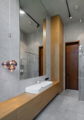 Interior of bathroom in luxury flat. Grey and wooden design. White sink.