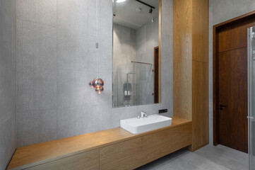 Interior of bathroom in luxury flat. Grey and wooden design. White sink.