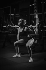 Fototapeta na wymiar A fit woman is squatting with a barbell near the squat rack in a gym.