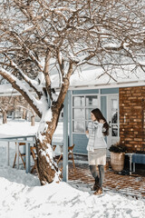 Woman is standing at a nice little house during winter at the morning.