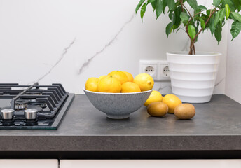 Bowl of citrus on dark kitchen counter with indoor plant. Modern kitchen interior. copy space