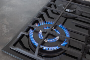 gas stove top with blue flame on dark countertop surface. Modern kitchen stove cook