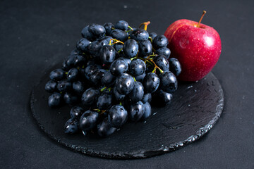 Fresh blue grapes on black plate and a bright red apple